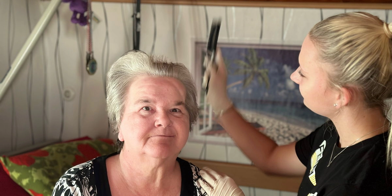 Eine junge Frau von einem Pflegedienst bei der Altenpflege. Sie kämmt einer alten Dame das Haar.