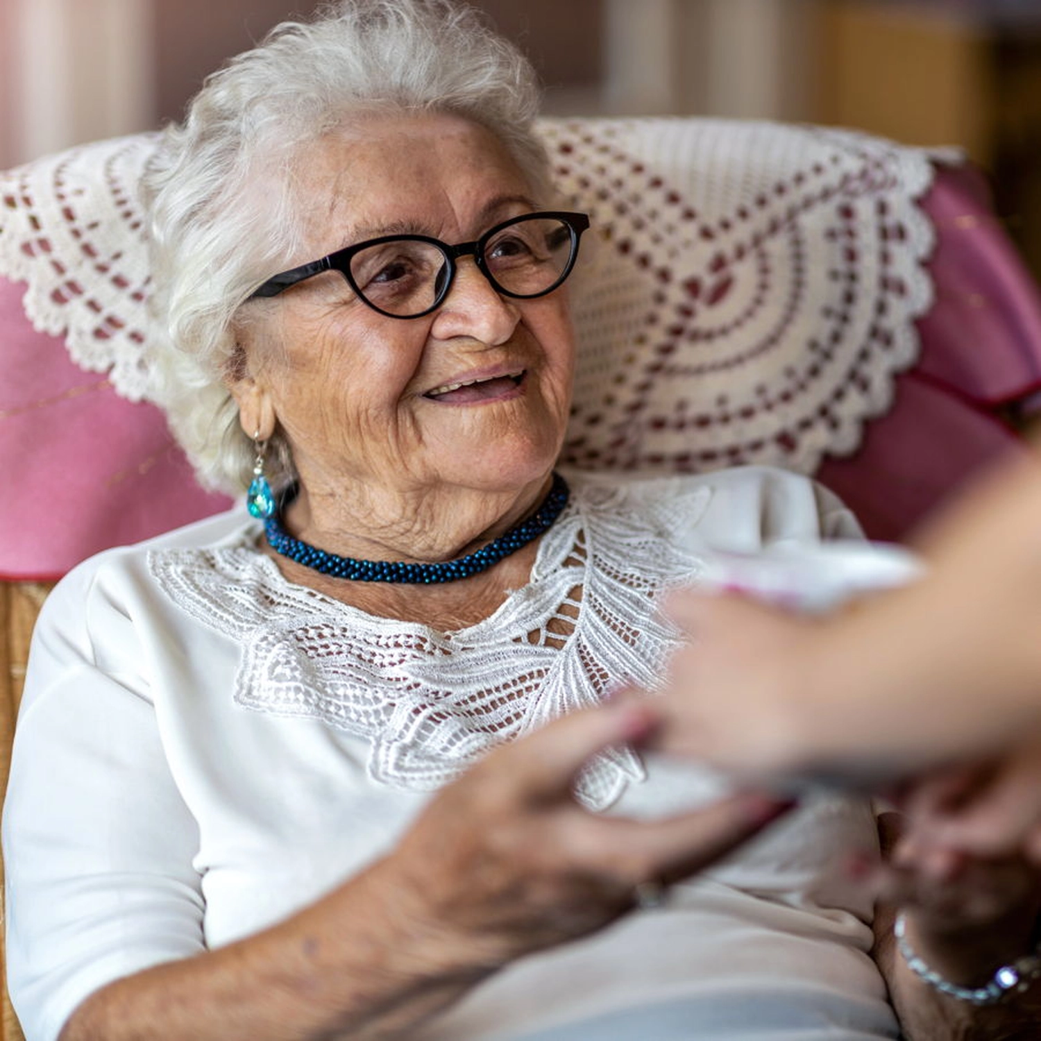 Eine freundliche ältere Dame bei einer Behandlungspflege, reicht den Pflegerinnen Ihre Hände.