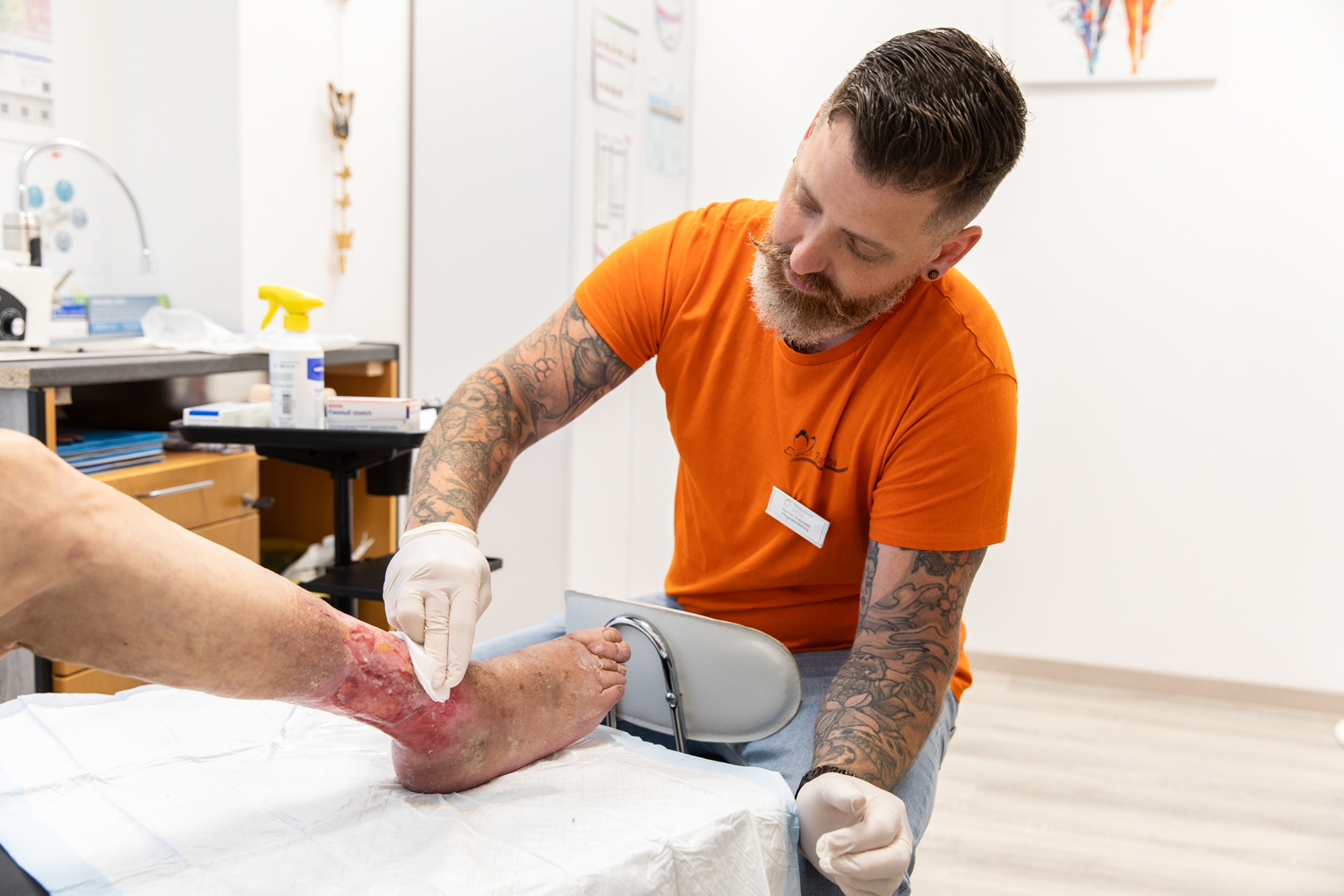Mann mit Handschuhen versorgt eine offene Wunde am Fuß eines Patienten in einer Praxis.