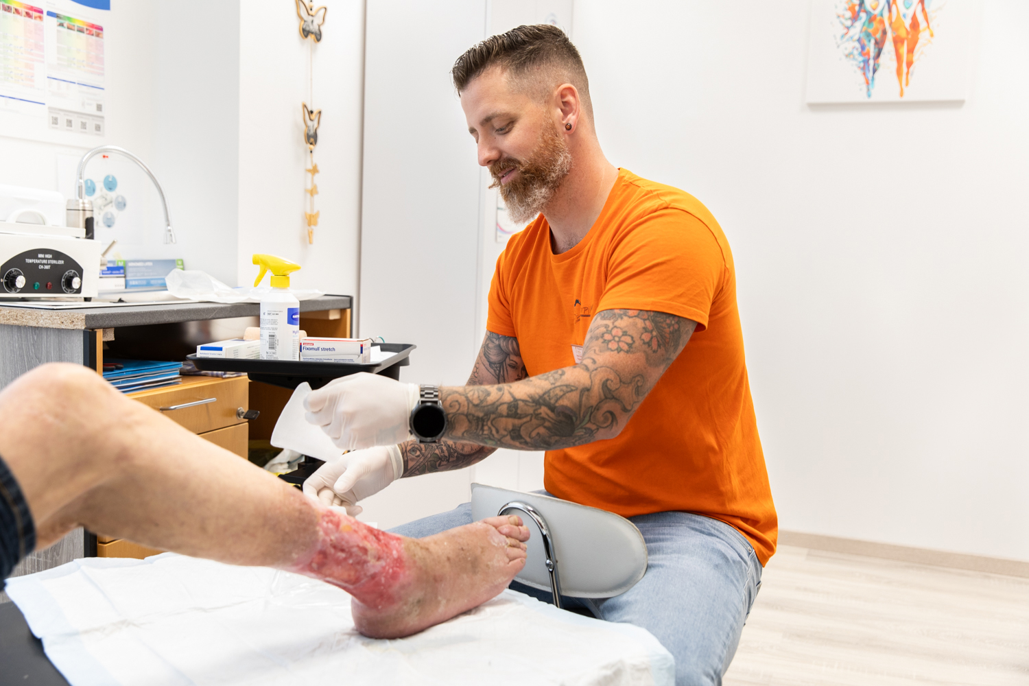 Ein medizinischer Fachmann vom Pflegedienst Papillon versorgt eine verletzte, gerötete Fuß- und Knöchelpartie eines Patienten.
